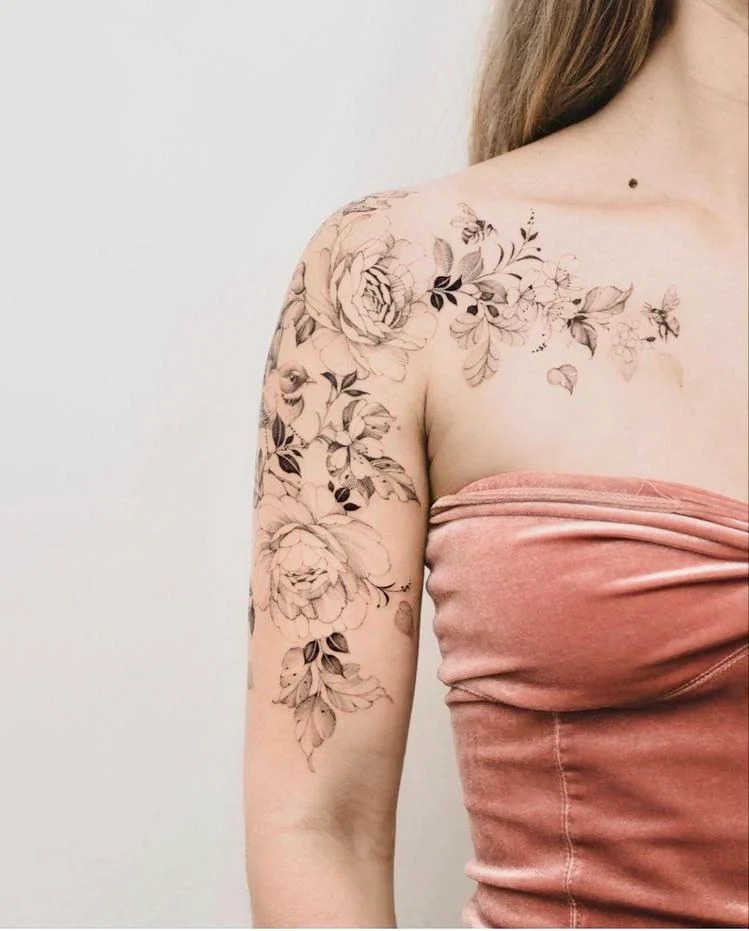 This tattoo features a gorgeous combination of large floral blooms and smaller botanical elements cascading over the shoulder and down the arm.