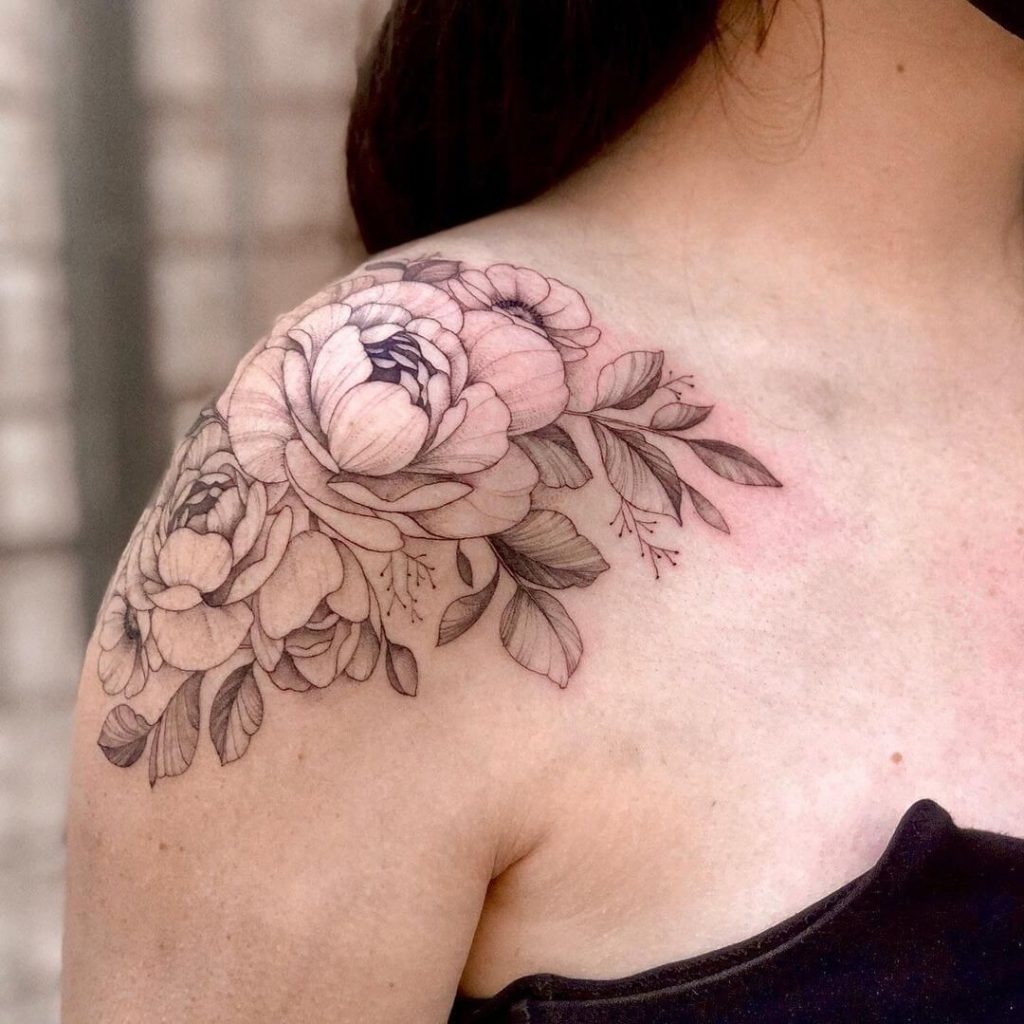 This floral shoulder cap tattoo offers a soft and artistic look, featuring peonies and smaller flowers cascading down the shoulder.