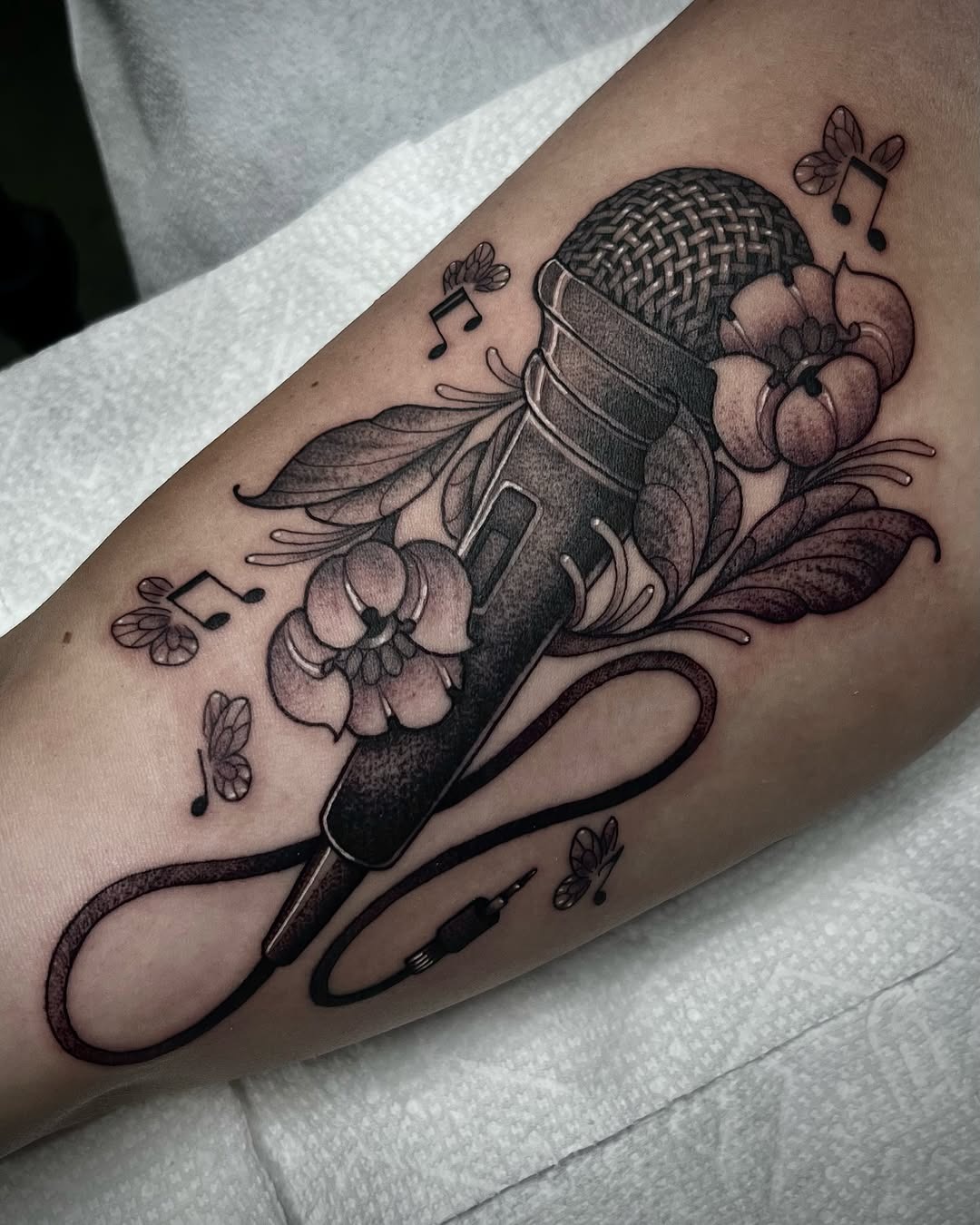 This stunning tattoo features a microphone entwined with beautiful flowers.