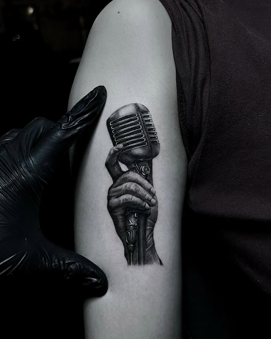 This tattoo features a detailed hand gripping a vintage microphone, showing remarkable shading and depth.