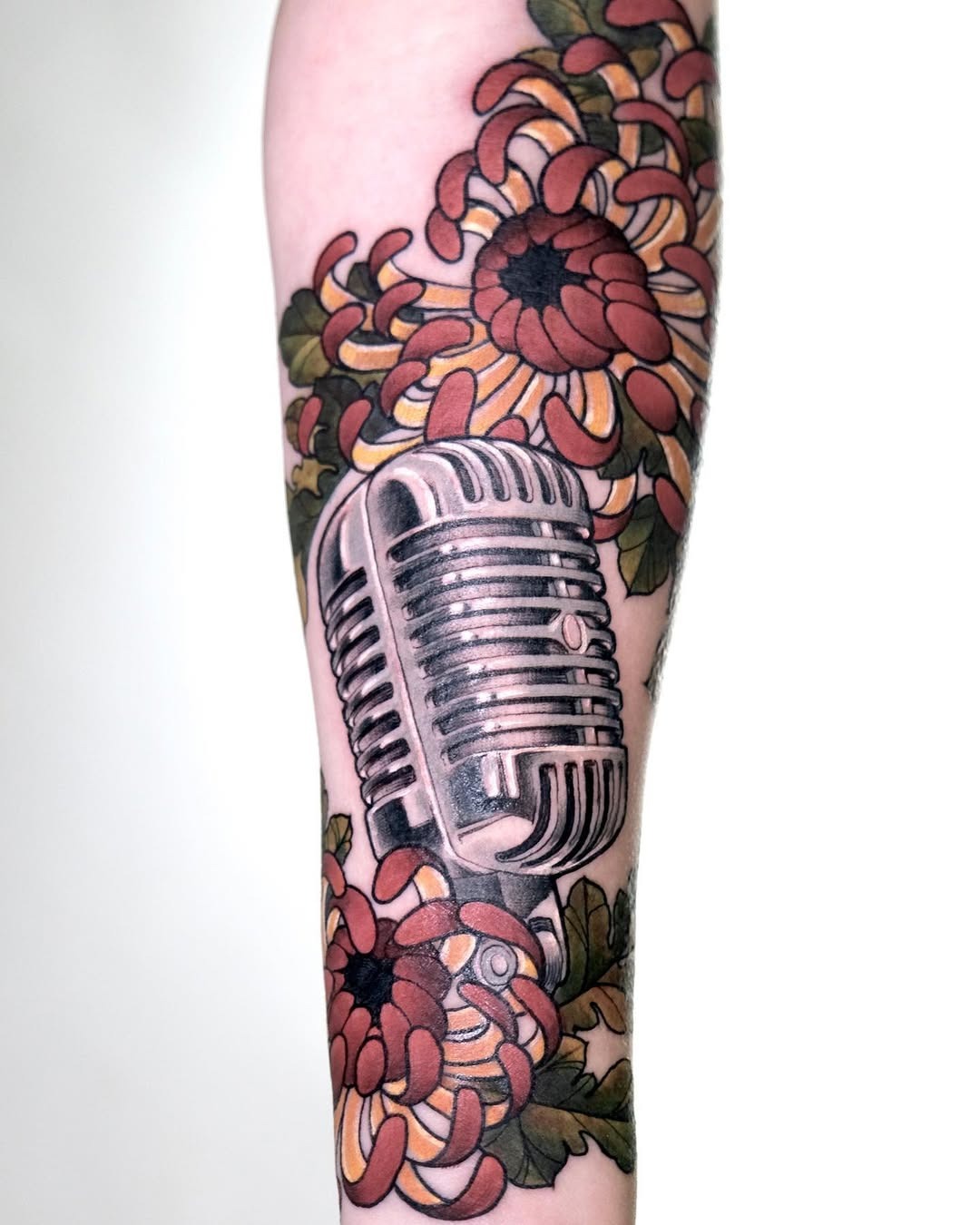 This microphone tattoo showcases a classic design intertwined with beautiful flowers.