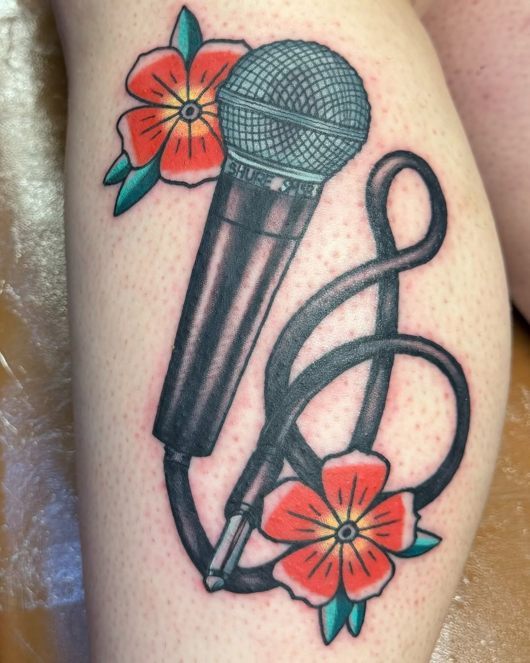 This microphone tattoo showcases a classic design intertwined with beautiful flowers.