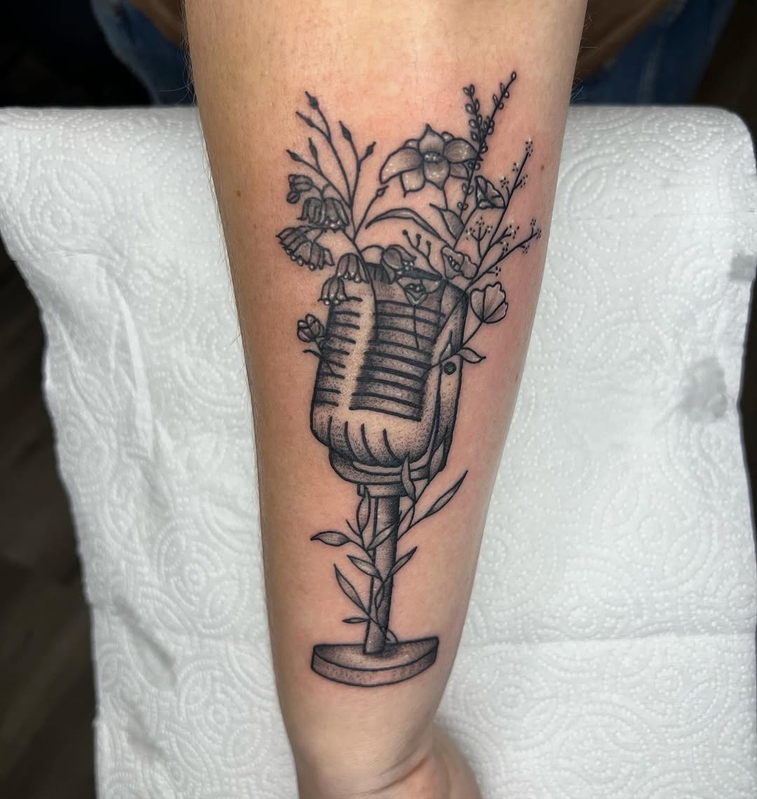 This tattoo features a vintage microphone entwined with delicate flowers.