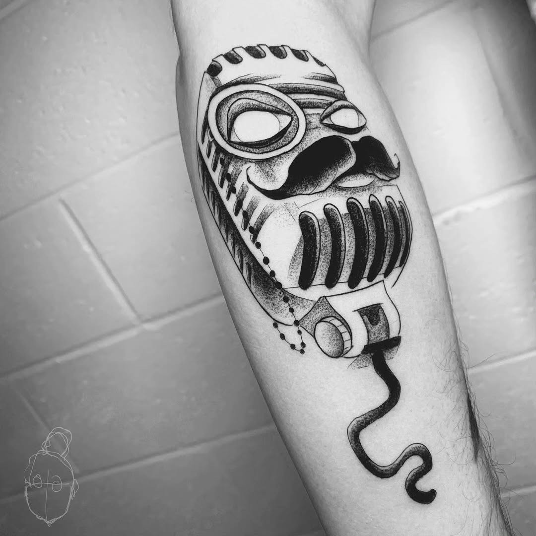 This tattoo showcases a striking vintage microphone illustrated with a whimsical mustache.