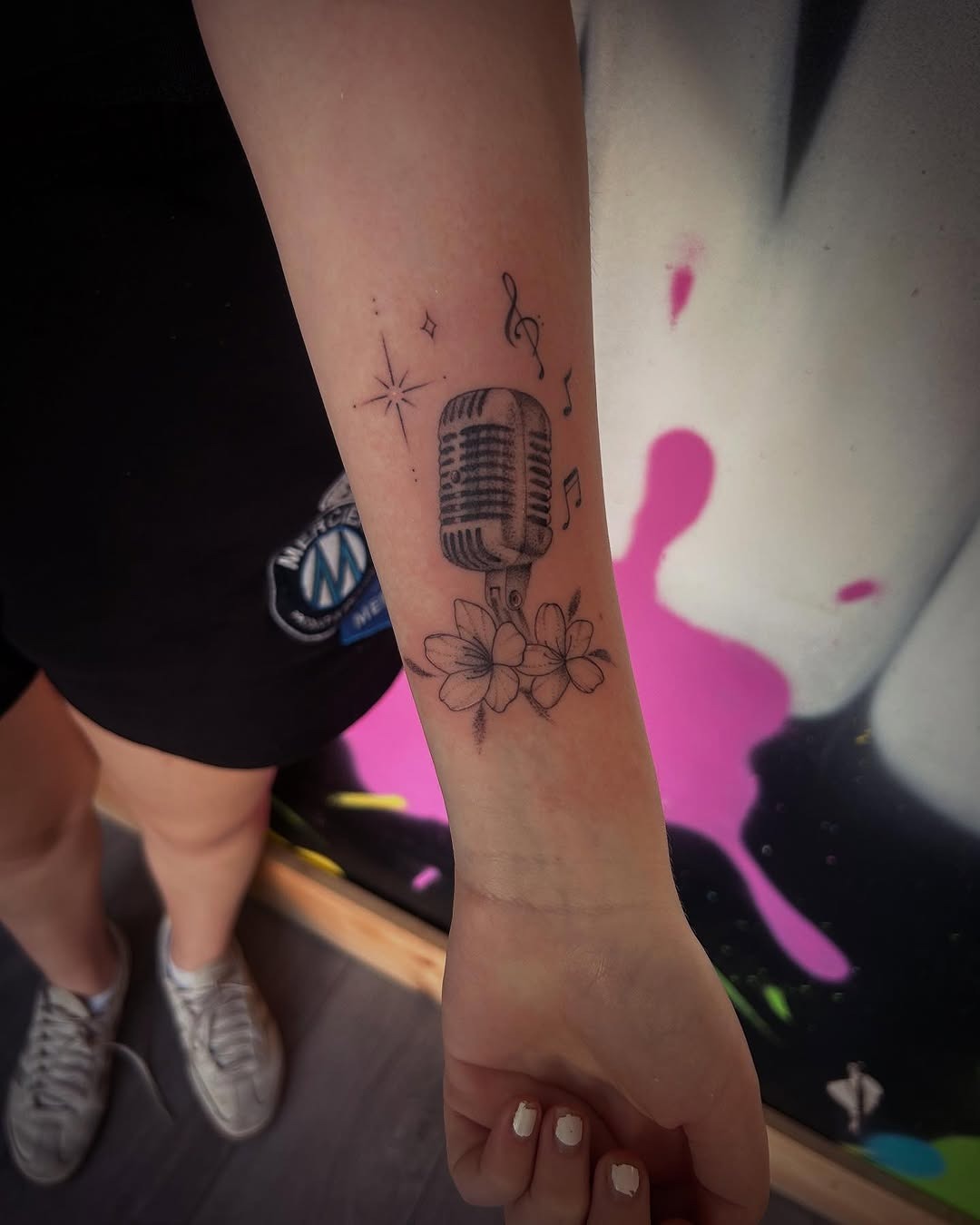 This tattoo features a vintage microphone surrounded by delicate flowers, signifying a love for music and nature.