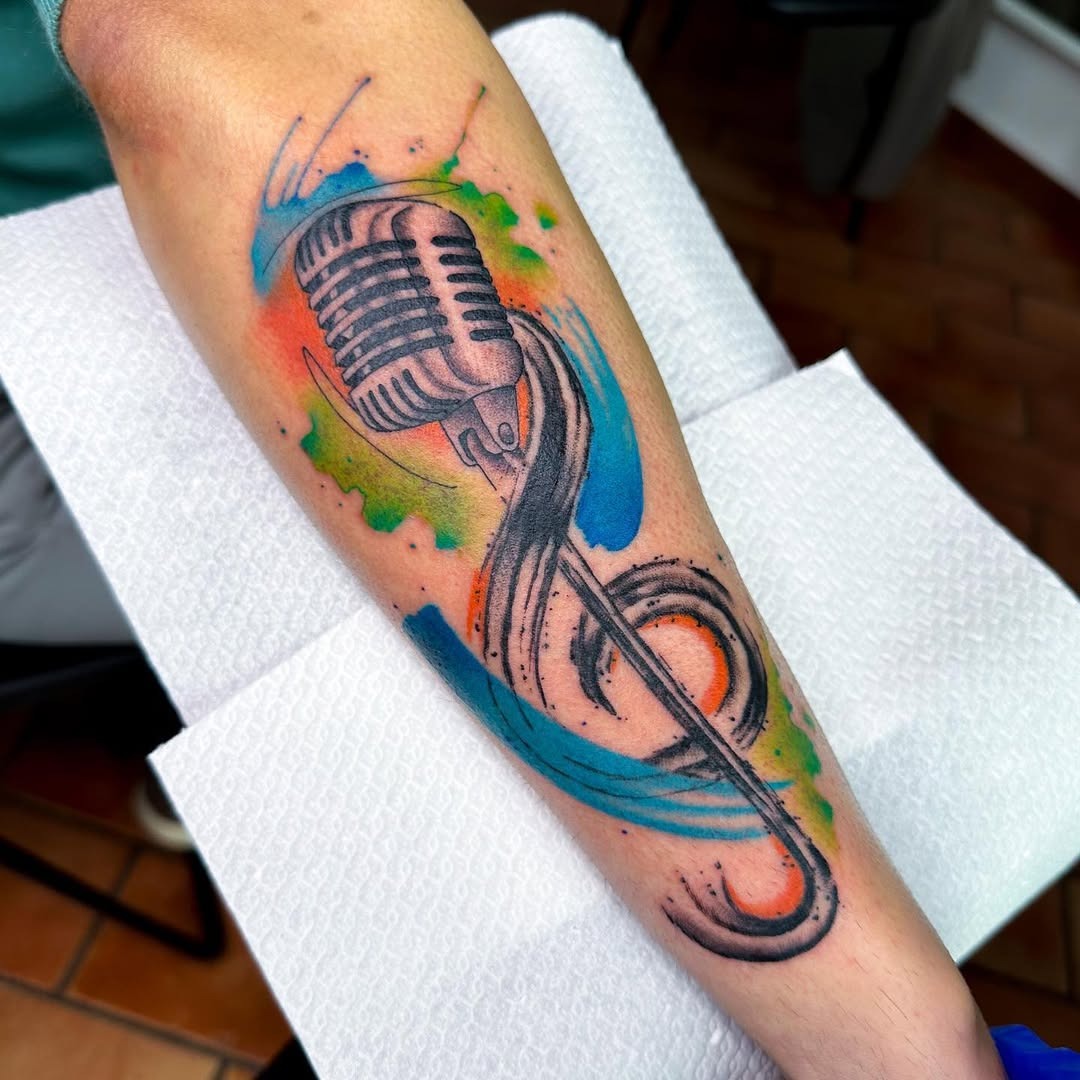 This tattoo features a classic microphone entwined with colorful swirls and splashes.
