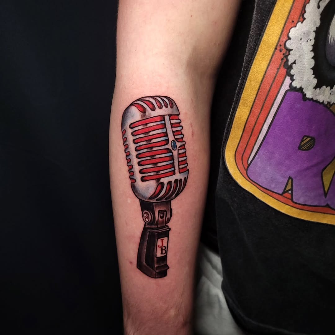 This tattoo showcases a classic vintage microphone design, featuring striking red accents that bring it to life.