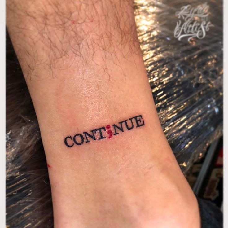 This minimalist tattoo features the word "CONTINUE," with the semicolon seamlessly replacing the letter "I." The placement on the ankle makes it a subtle yet empowering reminder of strength and perseverance.