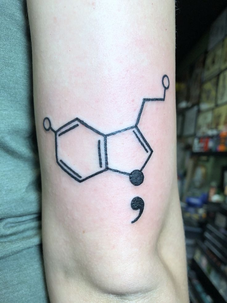 This tattoo integrates a serotonin molecule with a semicolon, making it a meaningful choice for those who advocate for mental health awareness.