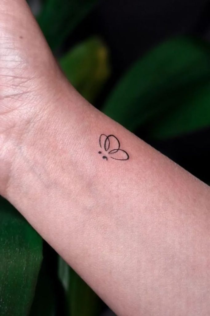 This delicate design blends a small butterfly with a semicolon, creating a soft and symbolic look.
