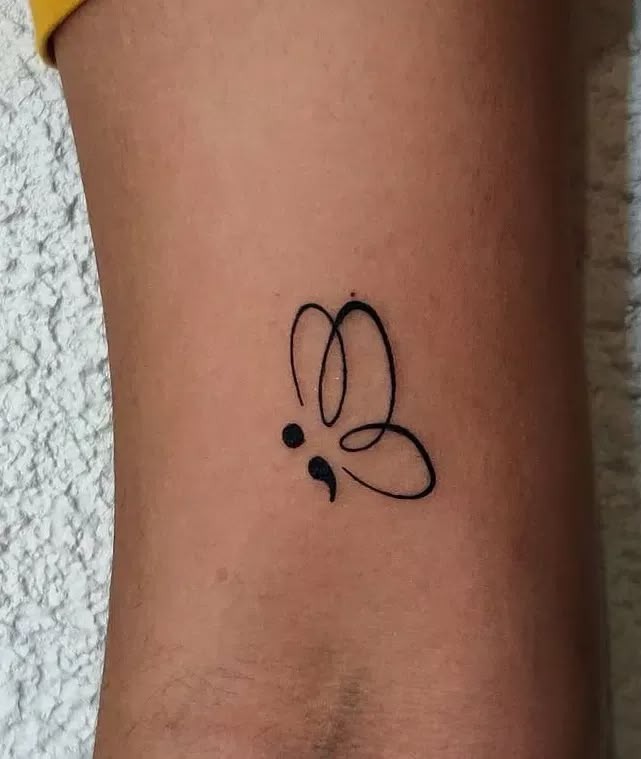 A small butterfly seamlessly integrated into a semicolon makes this an elegant and feminine tattoo choice.