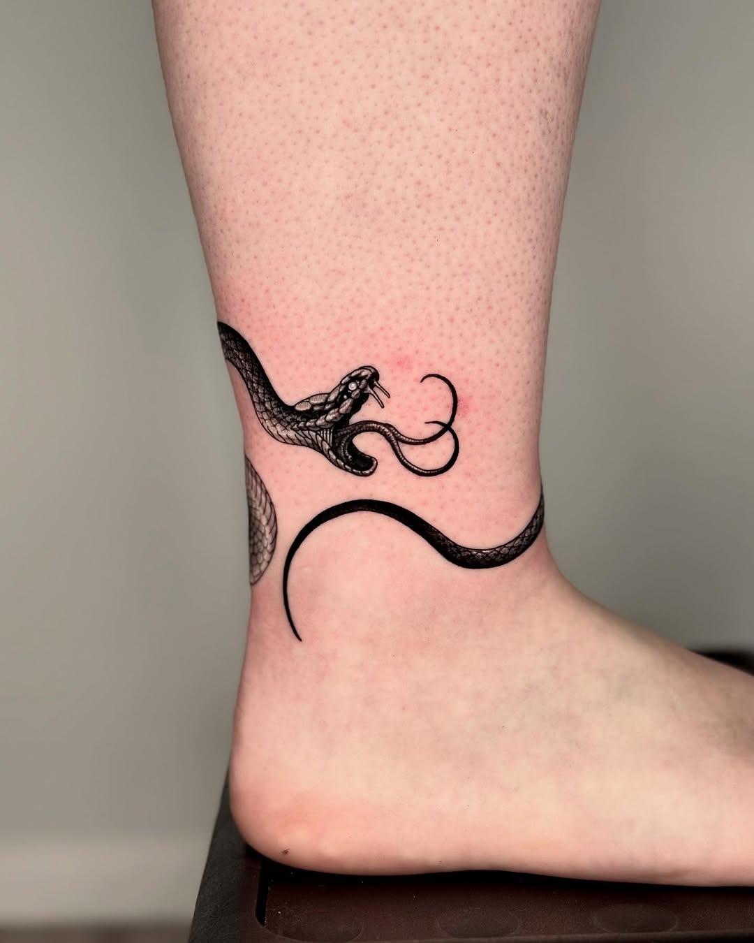 Elegant black snake tattoo on ankle area Tattoo Design