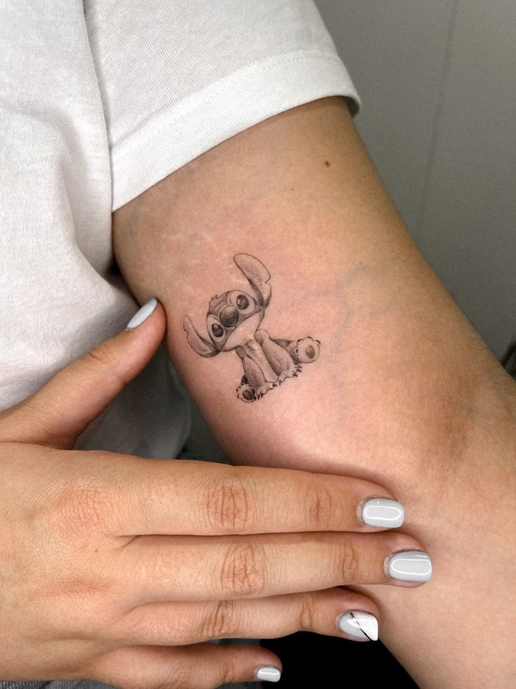 Tiny Shaded Stitch Upper Arm Tattoo, a tattoo design rendered in clean detailed linework.