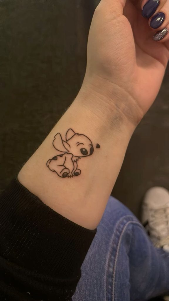 Tiny Sleeping Stitch Wrist Tattoo, a tattoo design rendered in clean detailed linework for the arm.