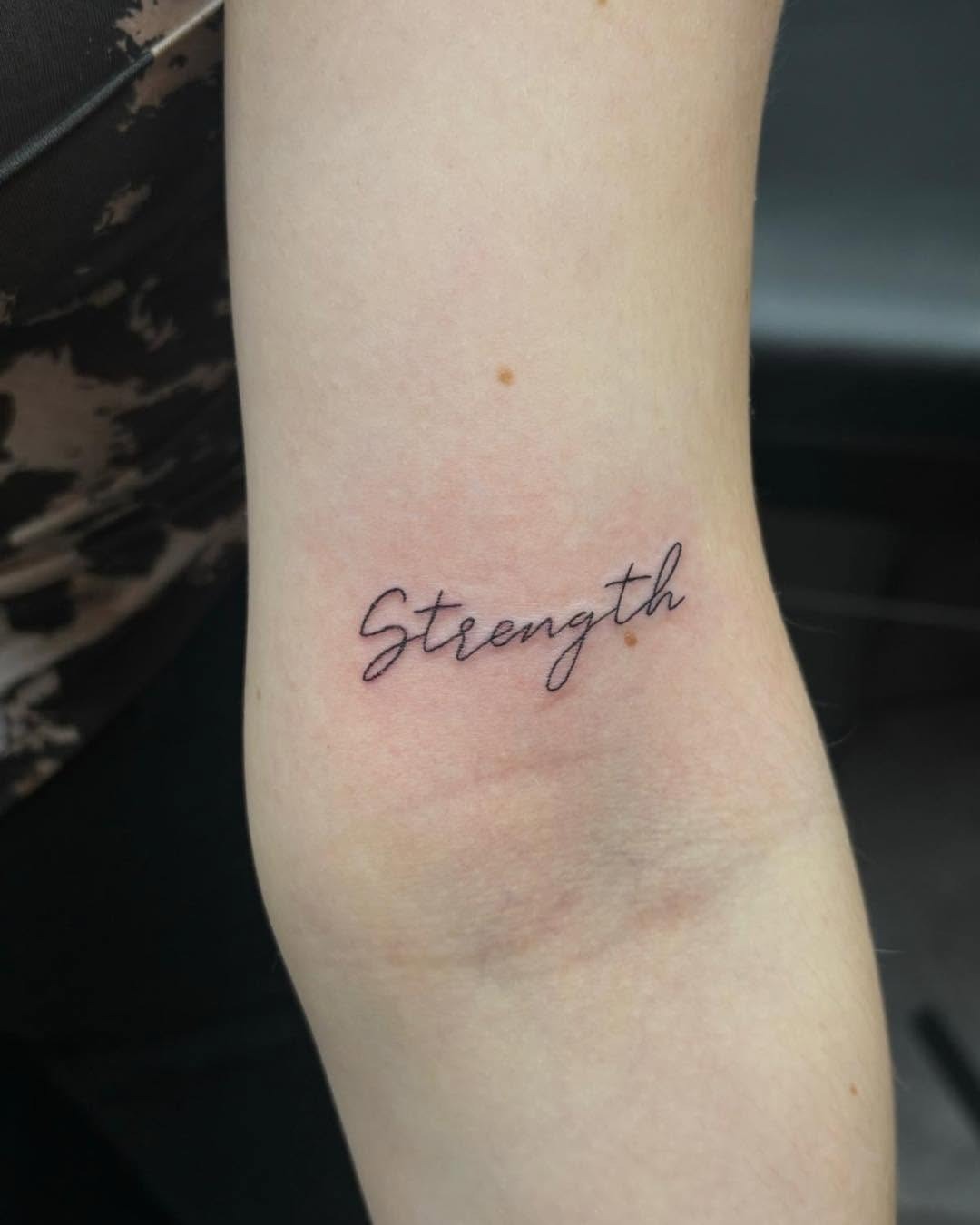 Meaningful strength tattoo featuring elegant strength tattoo in script font in bold black ink