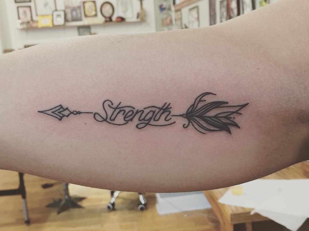 Meaningful strength tattoo featuring elegant strength tattoo with arrow motif in bold black ink