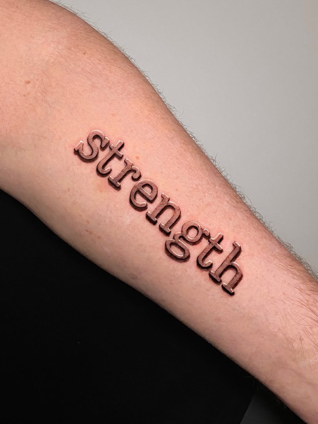 Meaningful strength tattoo featuring powerful strength tattoo on the forearm in bold black ink