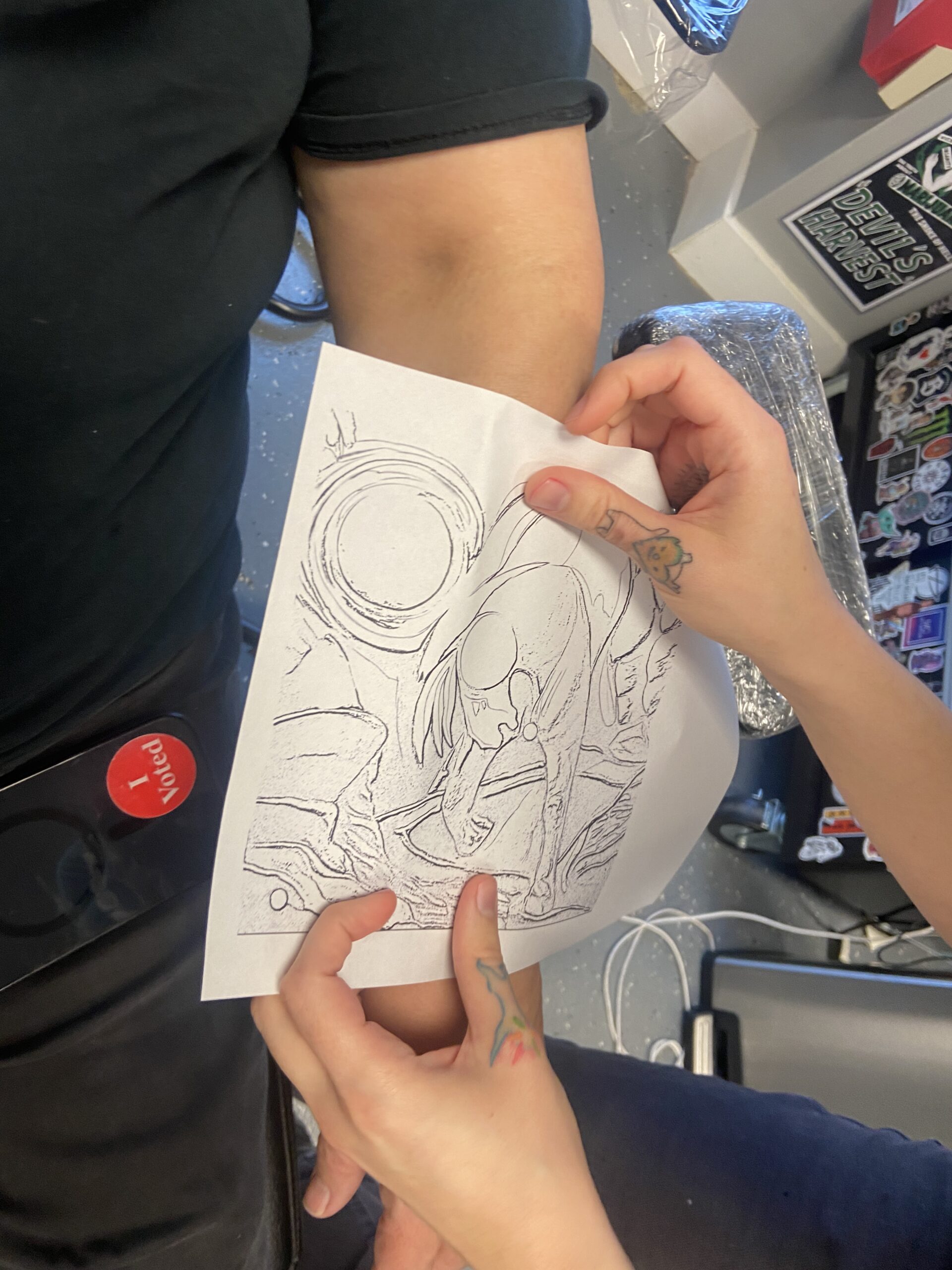 Tattoo artist checks the size of a printed design against a client's arm before transferring the stencil.