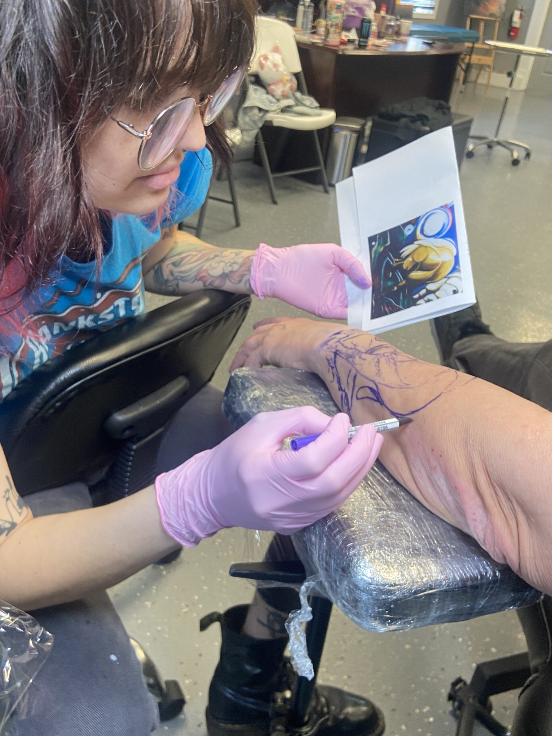 Tattoo artist making careful freehand adjustments to a stencil design before tattooing.