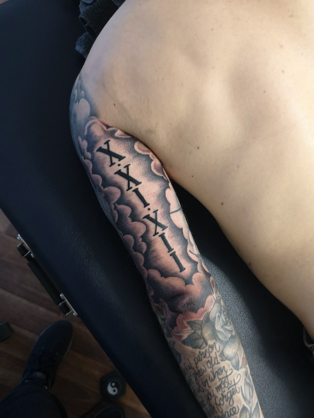 Roman Numeral Storm Clouds Tricep Tattoo, a tattoo design rendered in clean detailed linework.