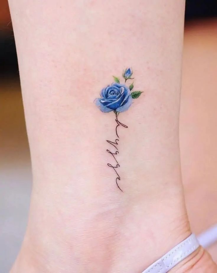 This tattoo combines a small blue rose with a delicate script that flows seamlessly from the stem.