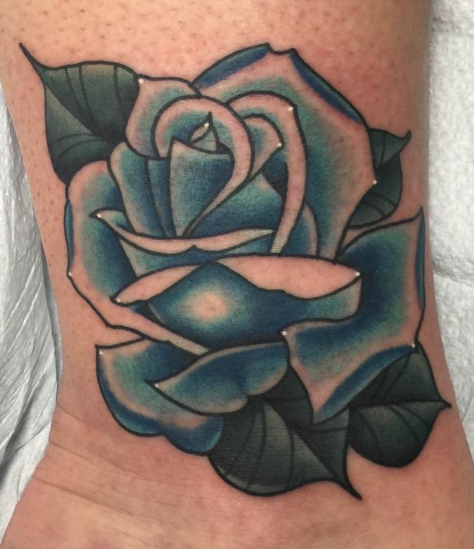 This ankle tattoo features a pair of blue roses surrounded by delicately shaded leaves.