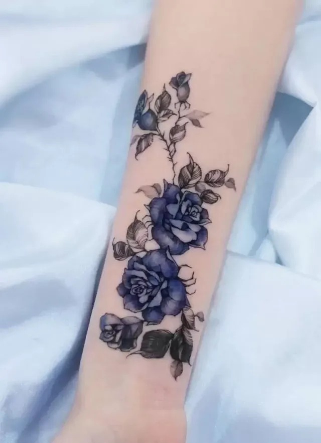 In this design, the blue roses cascade along the forearm in a beautiful vine pattern, adding a touch of nature-inspired elegance.