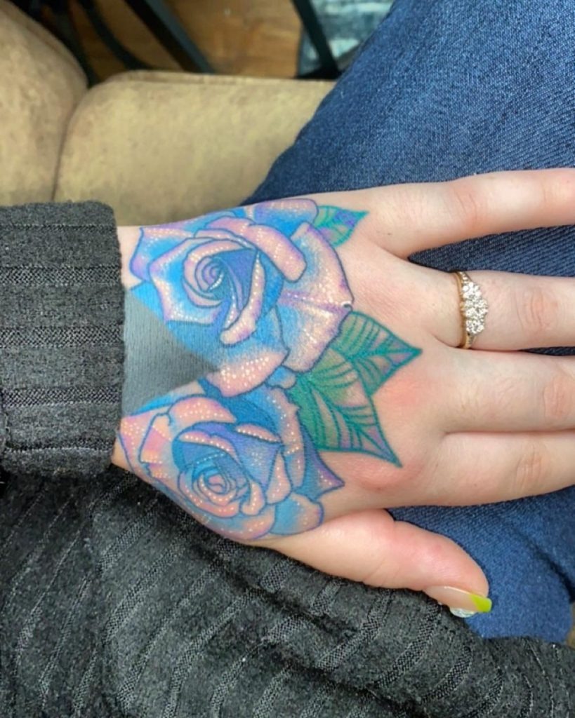 This hand tattoo features soft blue roses with a gentle touch of shimmer, perfect for those seeking a design that combines elegance with a hint of glamour.