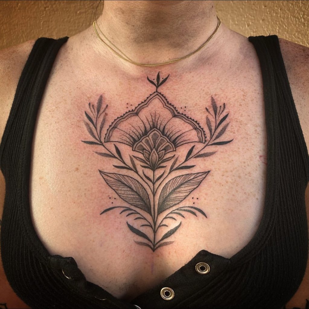 This tattoo combines elegance with nature-inspired artistry, featuring a floral design that rises from the sternum and fans out with leaf details.