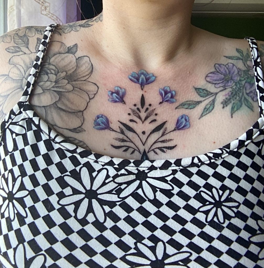 This chest tattoo stands out with its, blue-hued flowers that contrast with darker linework.