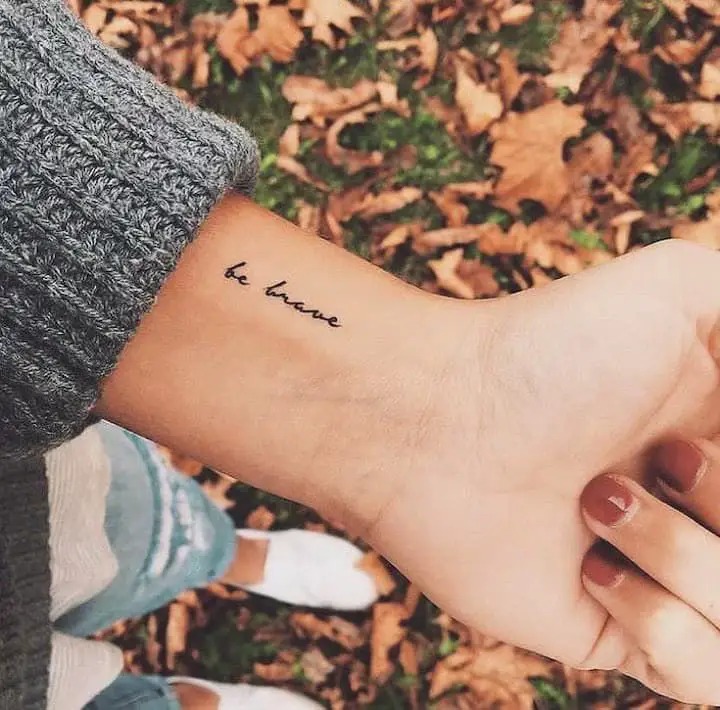 The phrase "be brave" is inked in a delicate, flowing script on the wrist, serving as a constant reminder to face life's challenges with courage.
