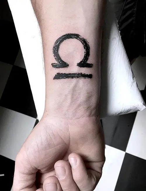 This bold tattoo showcases a brushstroke style Libra symbol, emphasizing strength and individuality.