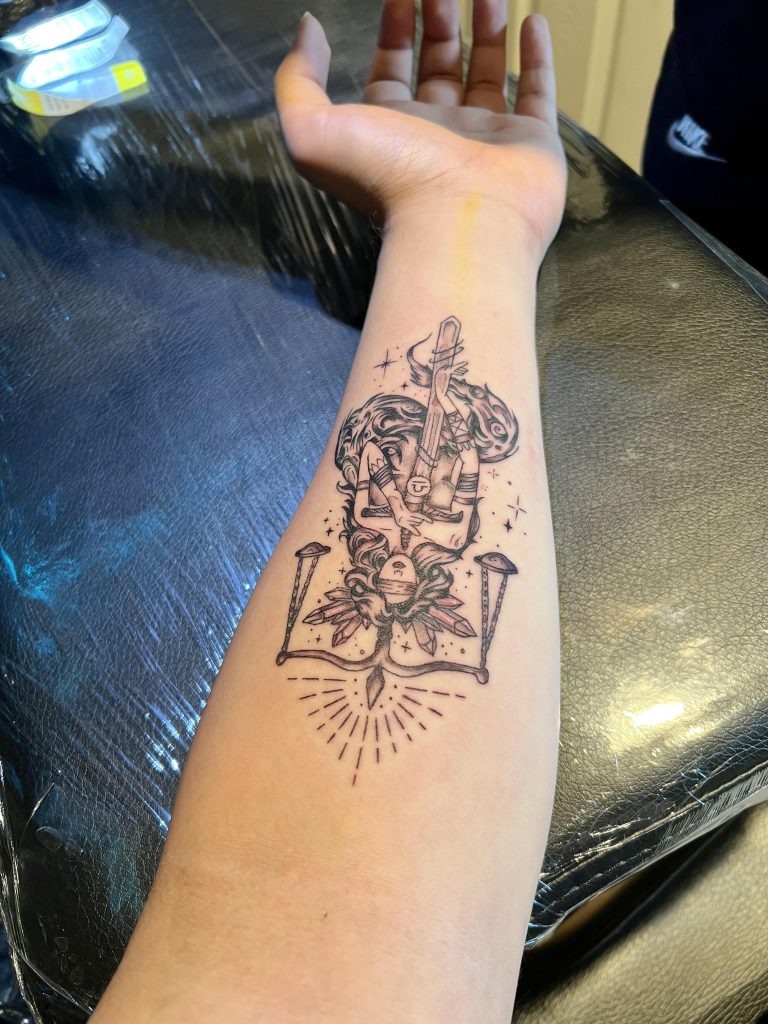 A highly detailed depiction of Lady Justice, blindfolded and holding a sword with scales balanced above her, graces this forearm tattoo.