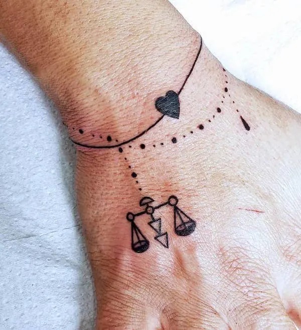 A perfect small tattoo idea for women, this wrist design offers a minimalist approach featuring the Libra symbol along with a delicate chain and heart motif.
