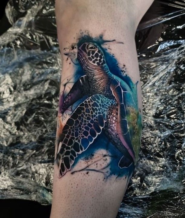 This tattoo combines a detailed watercolor aesthetic with a high level of detail in electric blue, seafoam green, and violet tones.