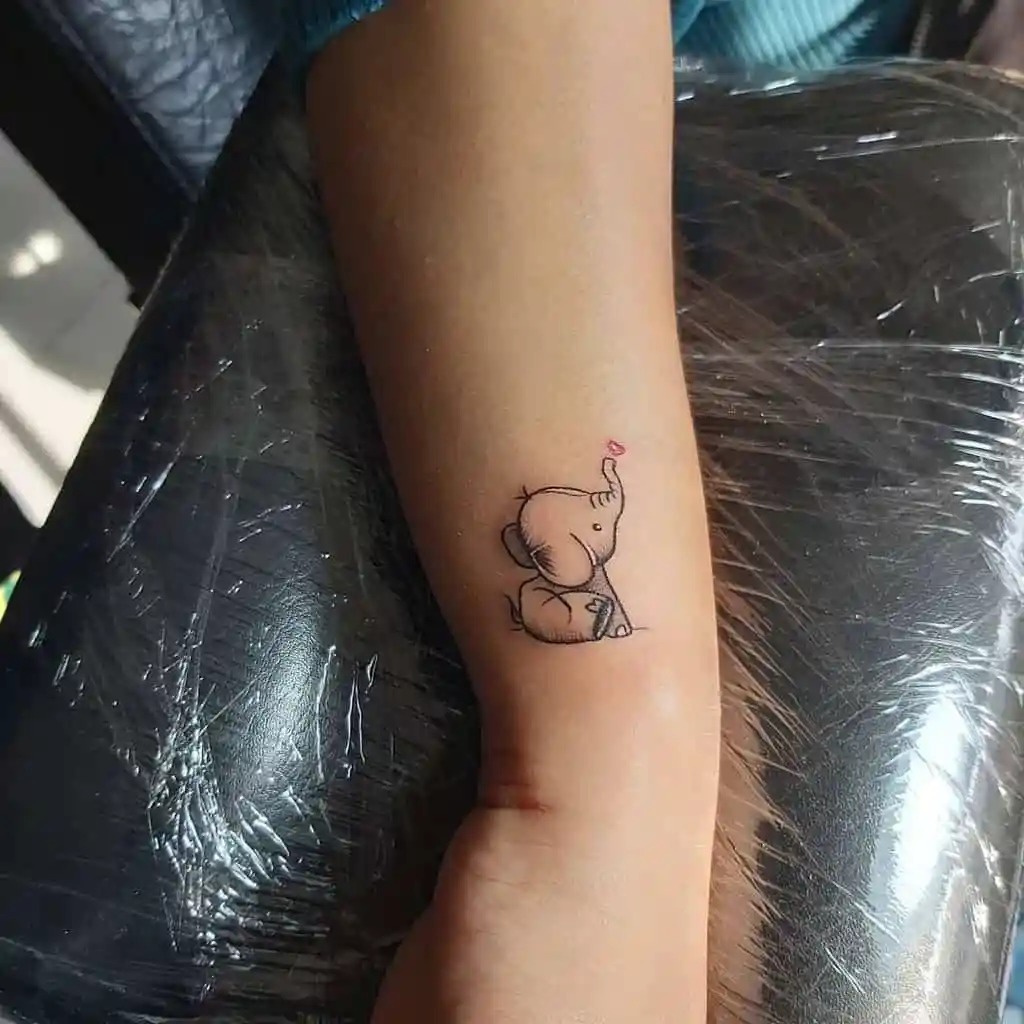 This adorable design depicts a baby elephant sitting with its trunk raised, symbolizing joy, positivity, and good luck.
