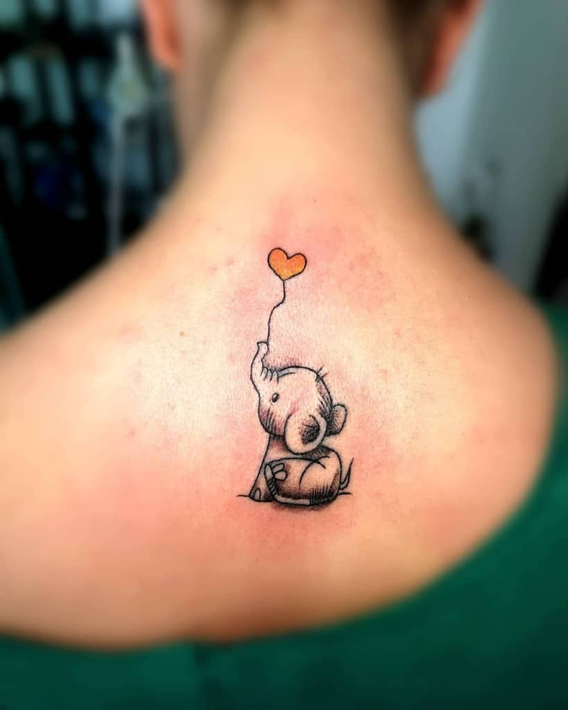 This heartwarming tattoo design shows a baby elephant sitting while holding a heart-shaped balloon.