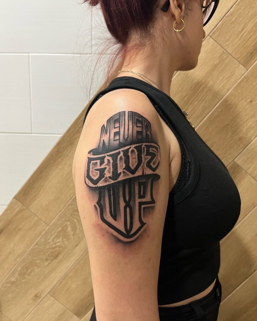 Bold "Never Give Up" Upper Arm Lettering Tattoo Tattoo Design